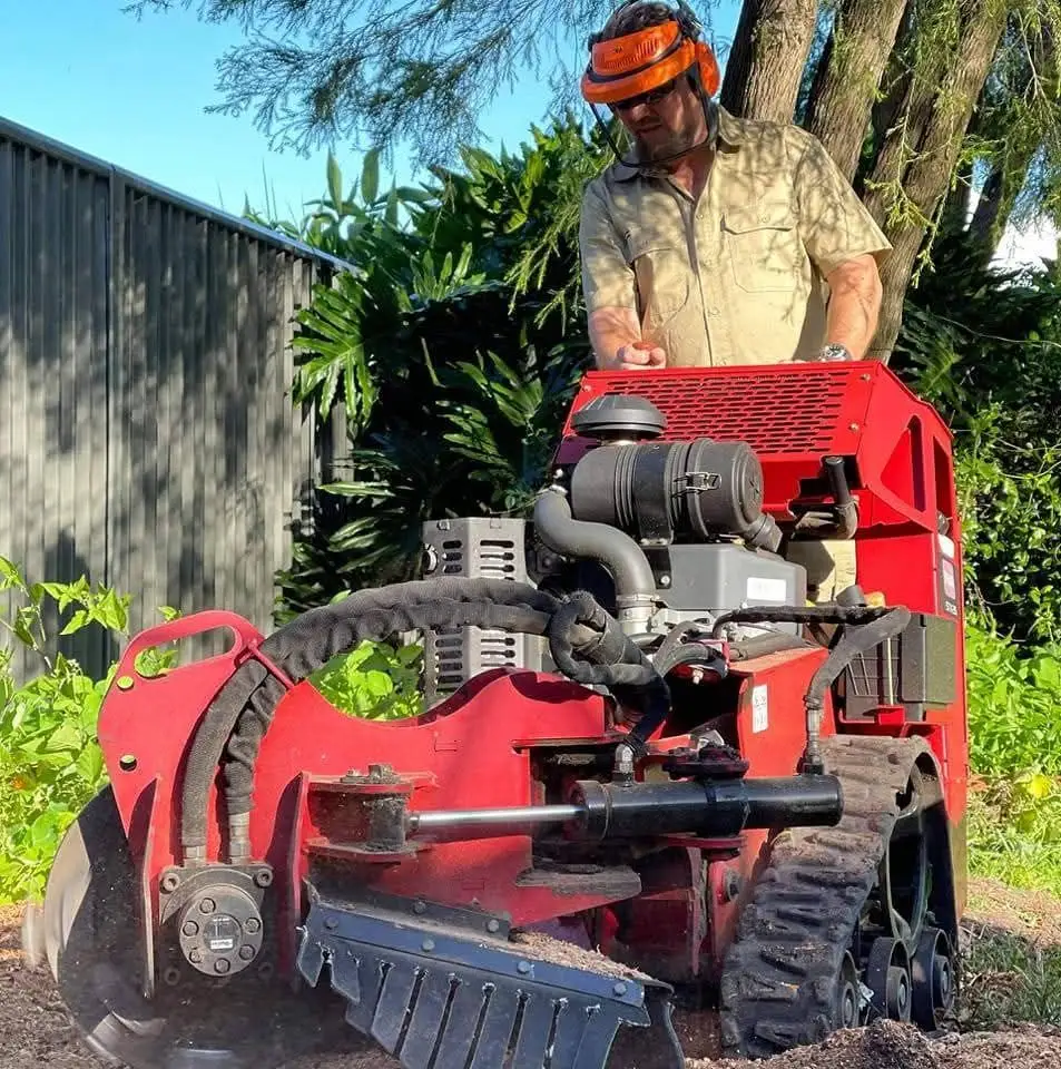 Paul in safety gear at the controls of the red tracked stump grinder